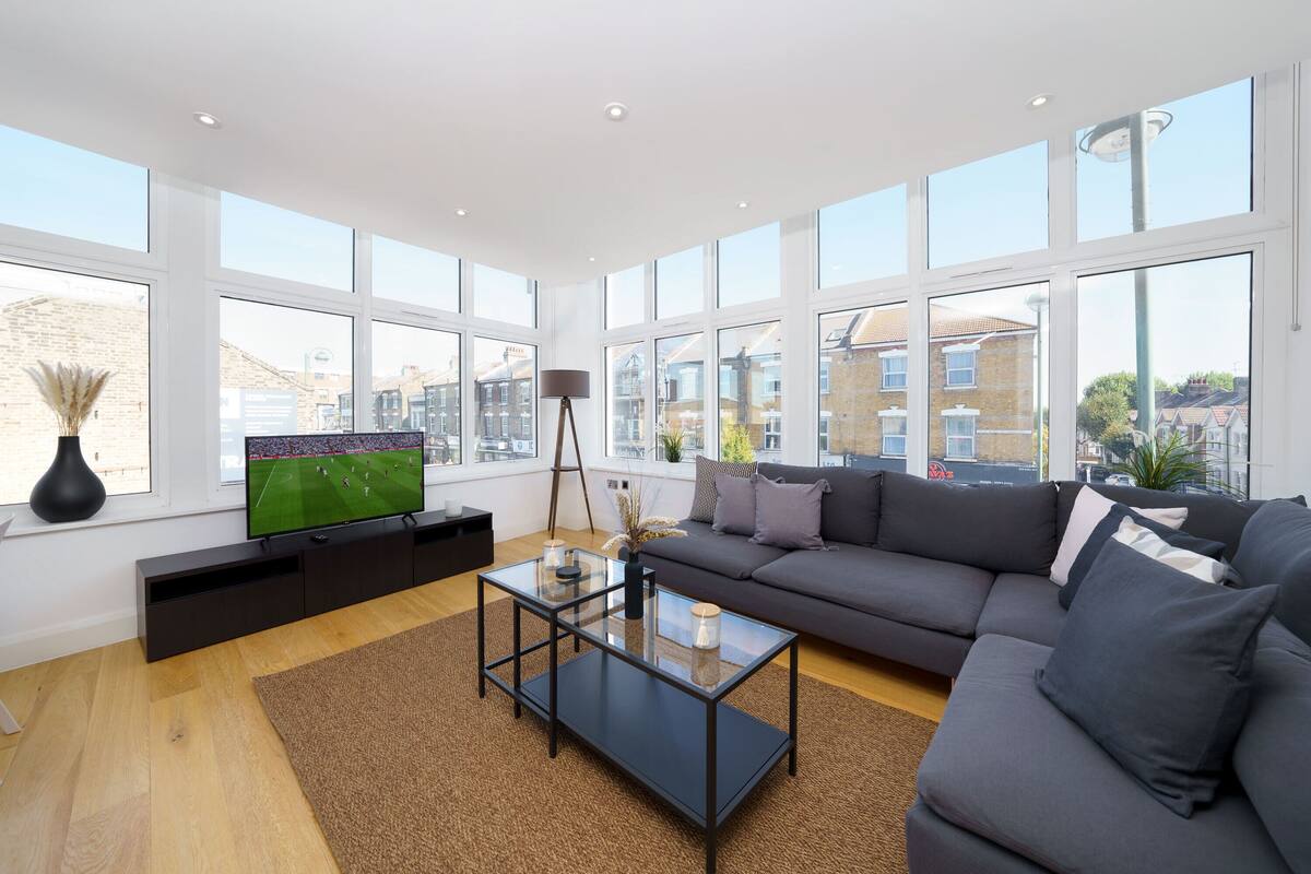 A modern living room with a large window, a flat-screen TV, a dark sofa, and a glass coffee table.