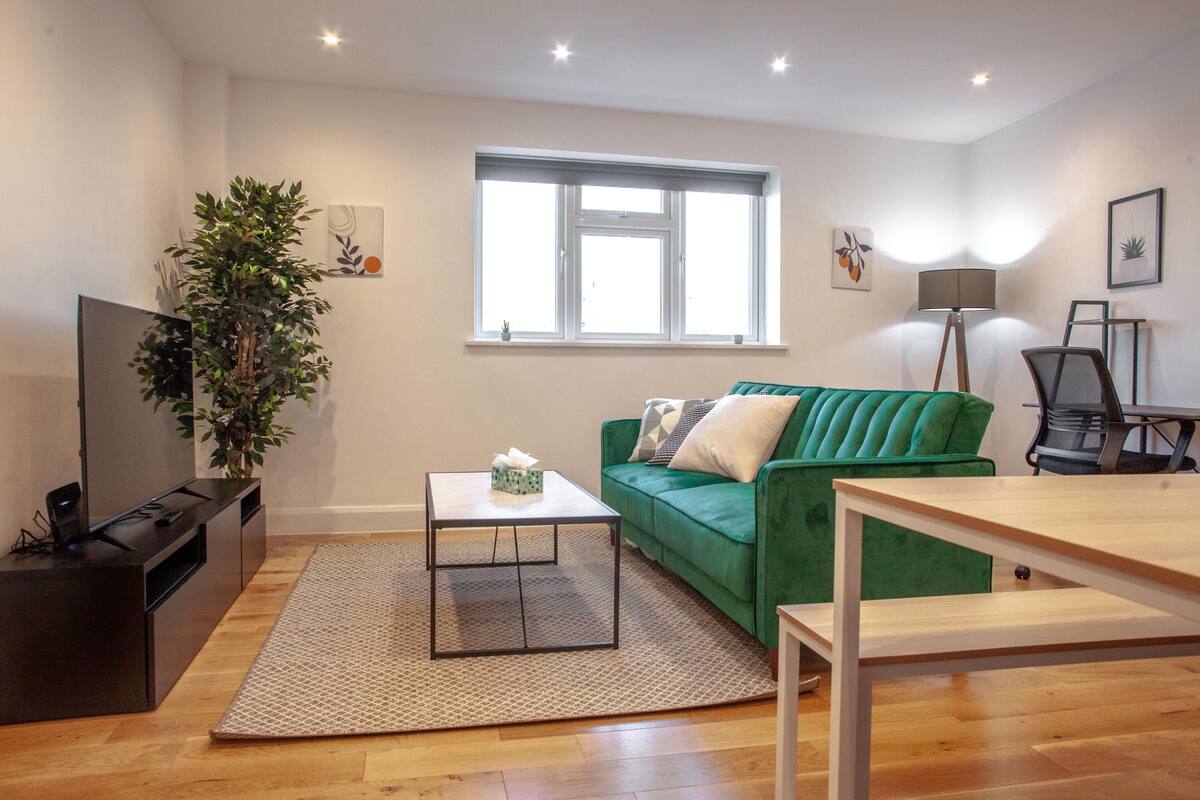 A modern living room with a green sofa, a coffee table, a TV, and a plant.