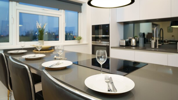 A modern kitchen with a large island, stainless steel appliances, and a view of the city at dusk. - Panther House by Oval (London)
