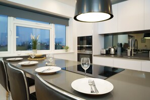 A modern kitchen with a large island, stainless steel appliances, and a view of the city at dusk. - Panther House by Oval (London)