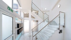 A modern interior with a glass staircase, a fire exit sign, and a row of storage boxes. - Panther House by Oval (London)
