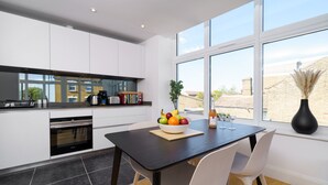 A modern kitchen with white cabinets, a black countertop, and a dining area with a black table and white chairs. - Panther House by Oval (London)