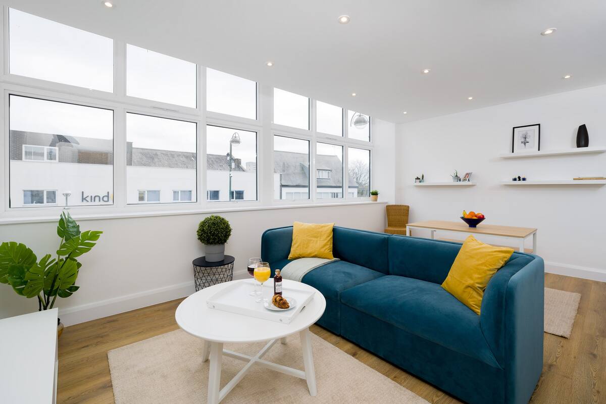 A modern living room with a blue sofa, white coffee table, and a large window with a view of buildings.
