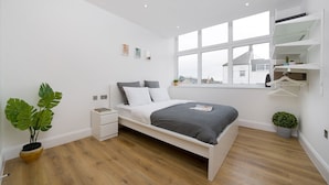 A modern bedroom with a bed, bedside tables, a window, and a potted plant. - Panther House by Oval (London)