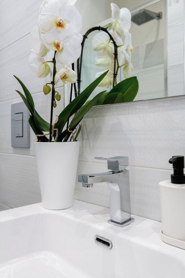 Ein Badezimmer mit einem weißen Waschbecken, einem modernen Wasserhahn und einer Topforchidee.