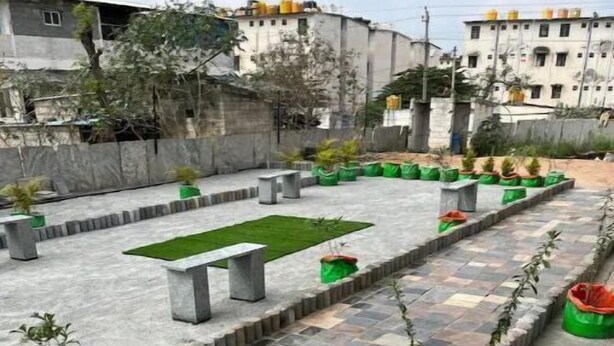 A rooftop garden with a checkered tile pathway, concrete bollards, and potted plants.