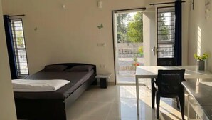 A bedroom with a bed, a desk, and a chair. There is a window and a door leading to an outdoor area.