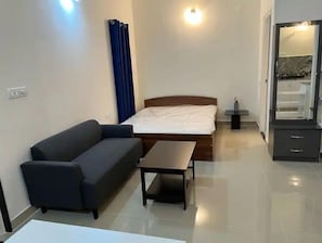 A hotel room with a bed, a sofa, a small table, a nightstand, and a mirror. - AZURE Whitefield, Studio B7, Serenity, Bliss & Relaxation (Bangalore)