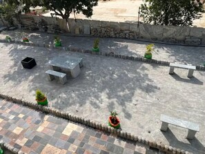 An outdoor patio area with a stone wall, a tiled floor, and several potted plants. - AZURE Whitefield, Studio B7, Serenity, Bliss & Relaxation (Bangalore)