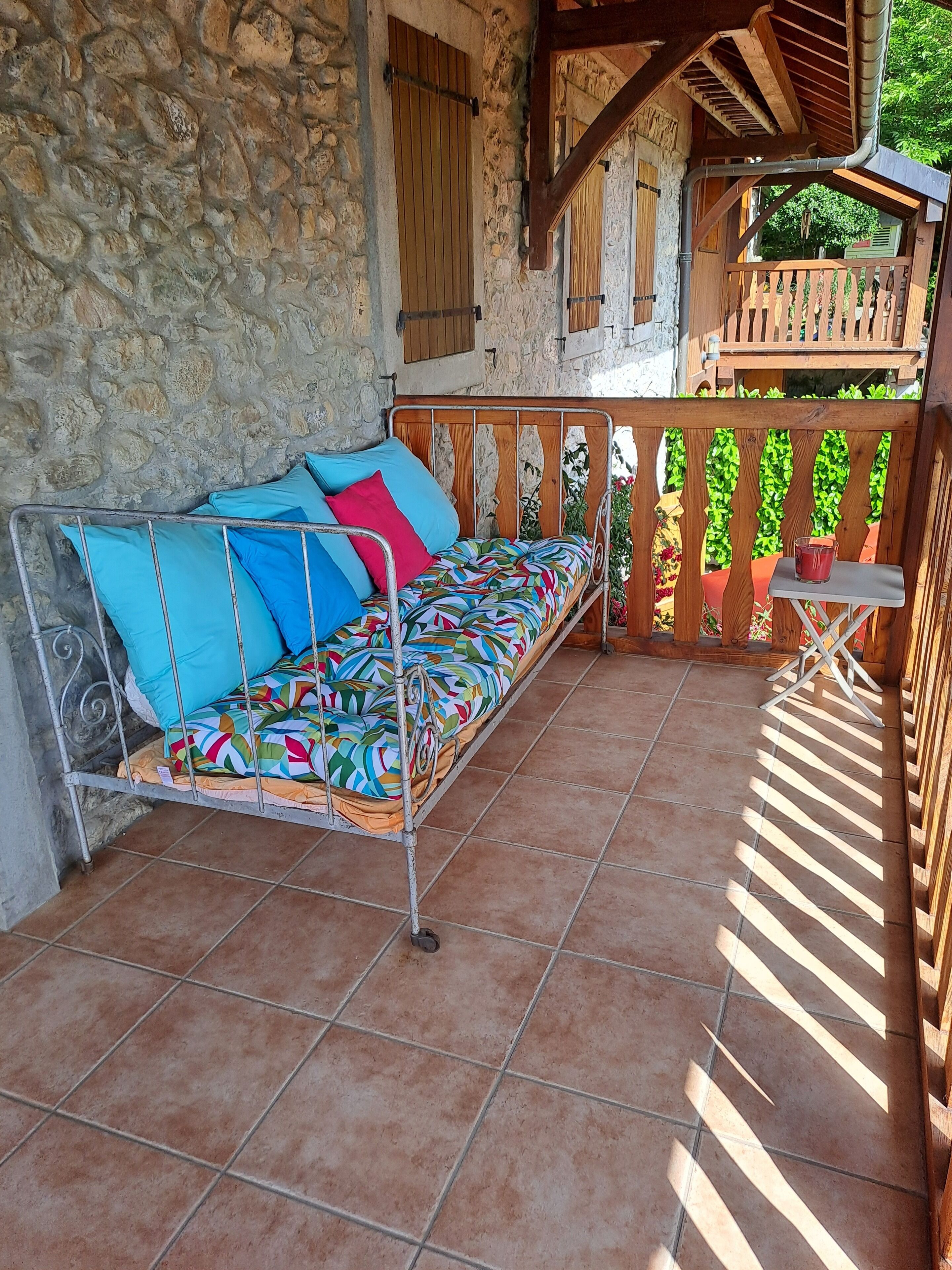 A metal bed with colorful bedding in a stone-walled room with a tiled floor.