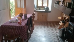 A dining area with a checkered tablecloth, wooden chairs, a window with a view, and a shelf with kitchen utensils. - LE RELAIS - LA FERME RÉDON  (Lugrin)