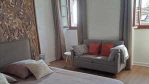 A bedroom with a large bed, a grey sofa, and a small table. - LE RELAIS - LA FERME RÉDON  (Lugrin)