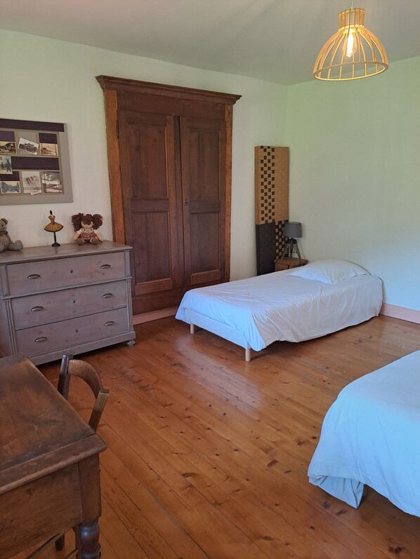 A bedroom with two single beds, a wooden dresser, a desk, a wooden wardrobe, a hanging light fixture, and a wall-mounted lamp. - LE RELAIS - LA FERME RÉDON (Lugrin)