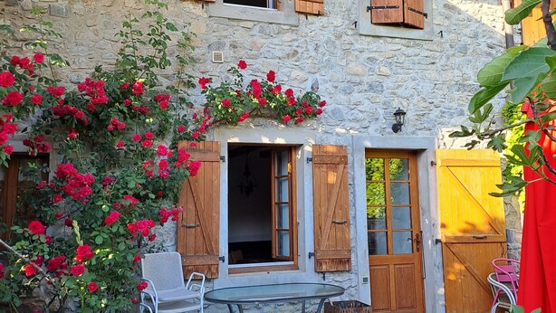 A stone building with wooden shutters, a glass table, and chairs outside. - LE RELAIS - LA FERME RÉDON  (Lugrin)