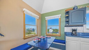 A kitchen with a blue bench seating area, a coffee maker, and a view of houses through the windows. - Oceanfront Dog Friendly Home with Hot Tub, Game Room, and Direct Beach Access (Avon)