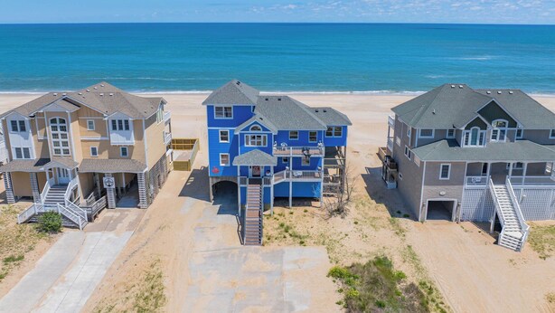 A beachfront property with multiple houses, a sandy beach, and the ocean in the background. - Oceanfront Dog Friendly Home with Hot Tub, Game Room, and Direct Beach Access (Avon)