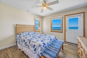 A bedroom with a bed, a ceiling fan, a bench, and a view of the ocean through two windows. - Oceanfront Dog Friendly Home with Hot Tub, Game Room, and Direct Beach Access (Avon)