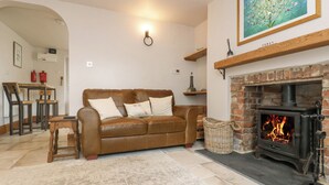 A cozy living room with a brown leather sofa, a fireplace, and a painting on the wall. - Woodbine Cottage (Falmouth)