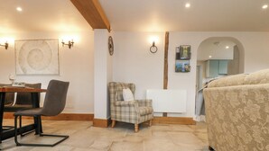 A cozy room with a dining table, a plaid armchair, a sofa, and a radiator. - Woodbine Cottage (Falmouth)