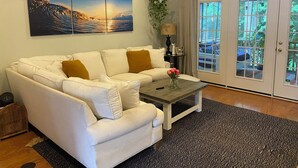 Ein Wohnzimmer mit einem weißen Sofa, einem Couchtisch und einem großen Fenster mit Blick ins Freie.