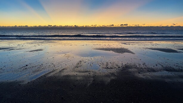 Ein Strand mit Wellen und einem Sonnenuntergang.