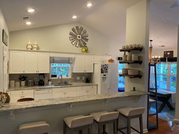 A modern kitchen with white cabinets, a granite countertop, and a large decorative clock on the wall.