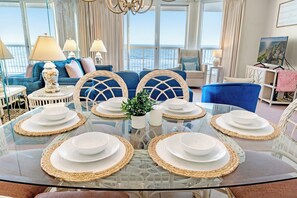 A dining area with a glass table set for six, surrounded by blue upholstered chairs with woven backs. - Ocean Front 3 BD/3 BA - Sunrise Pointe 4E (North Myrtle Beach)