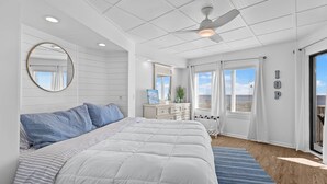 Quarto com cama grande, ventilador de teto, cômoda e janela com cortinas.