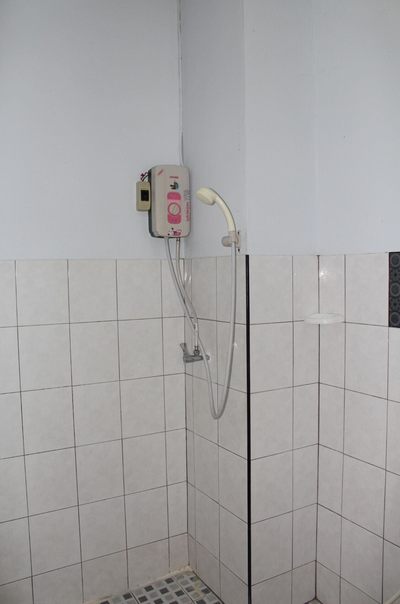 A small, tiled shower area with a handheld showerhead and a control panel.