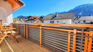 Ein Balkon mit Holzstuhl und Grill, mit Blick auf einen Berg und traditionelle Gebäude.