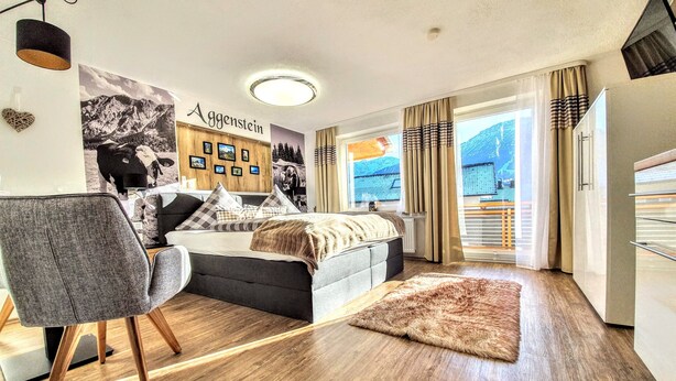 Ein modernes Schlafzimmer mit Bett, Sessel, Teppich und Wandgemälde.