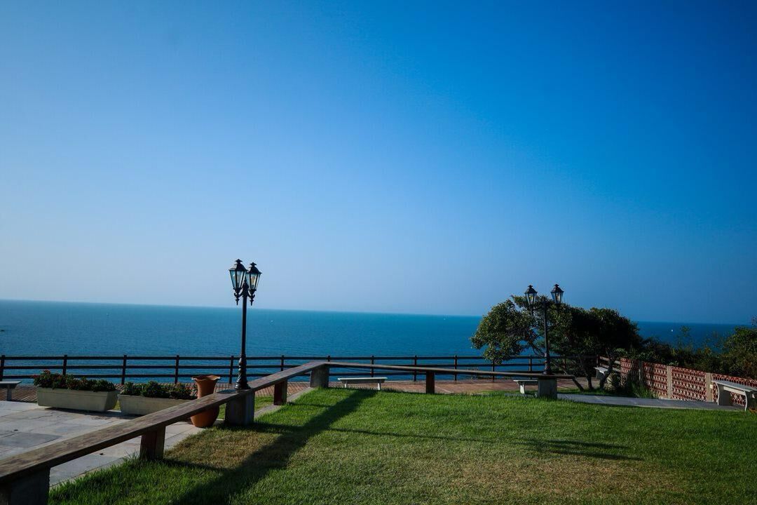 A coastal park with a wooden bench, lamp post, and a view of the sea.