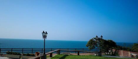 A coastal park with a wooden bench, lamp post, and a view of the sea.