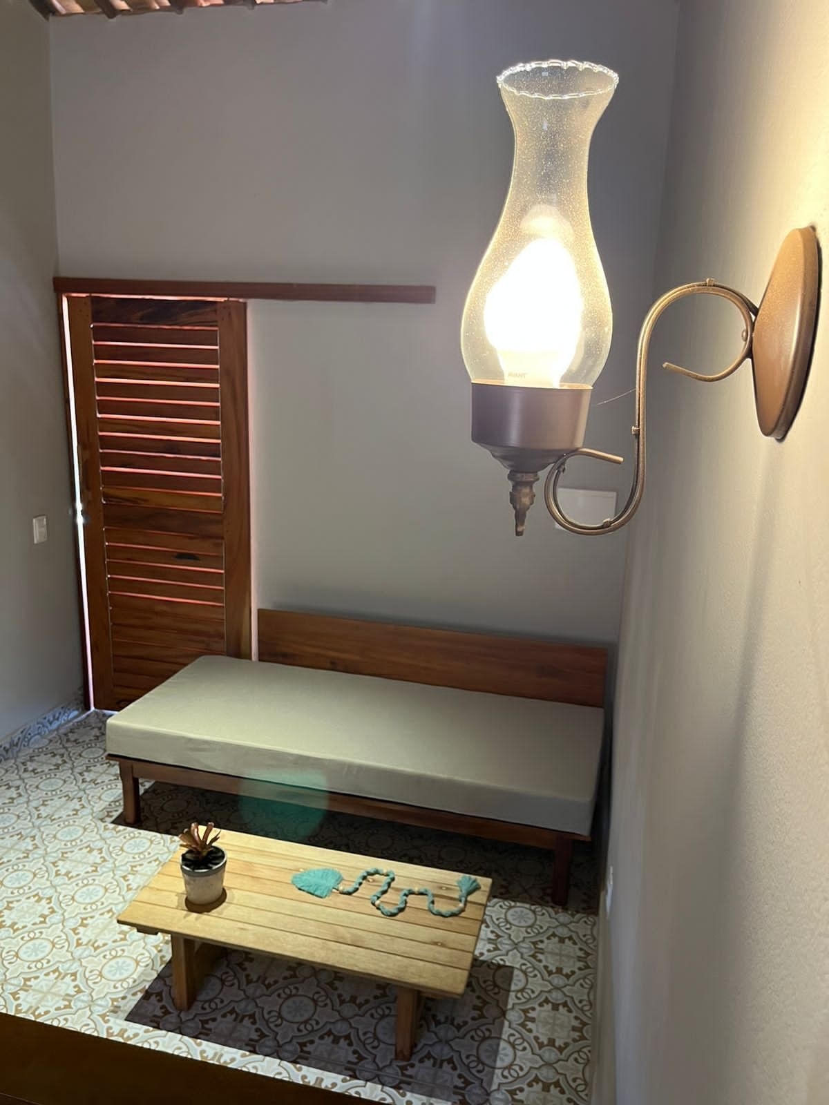 Una habitación pequeña y acogedora con un banco de madera, una mesita con una planta y un aplique de pared.