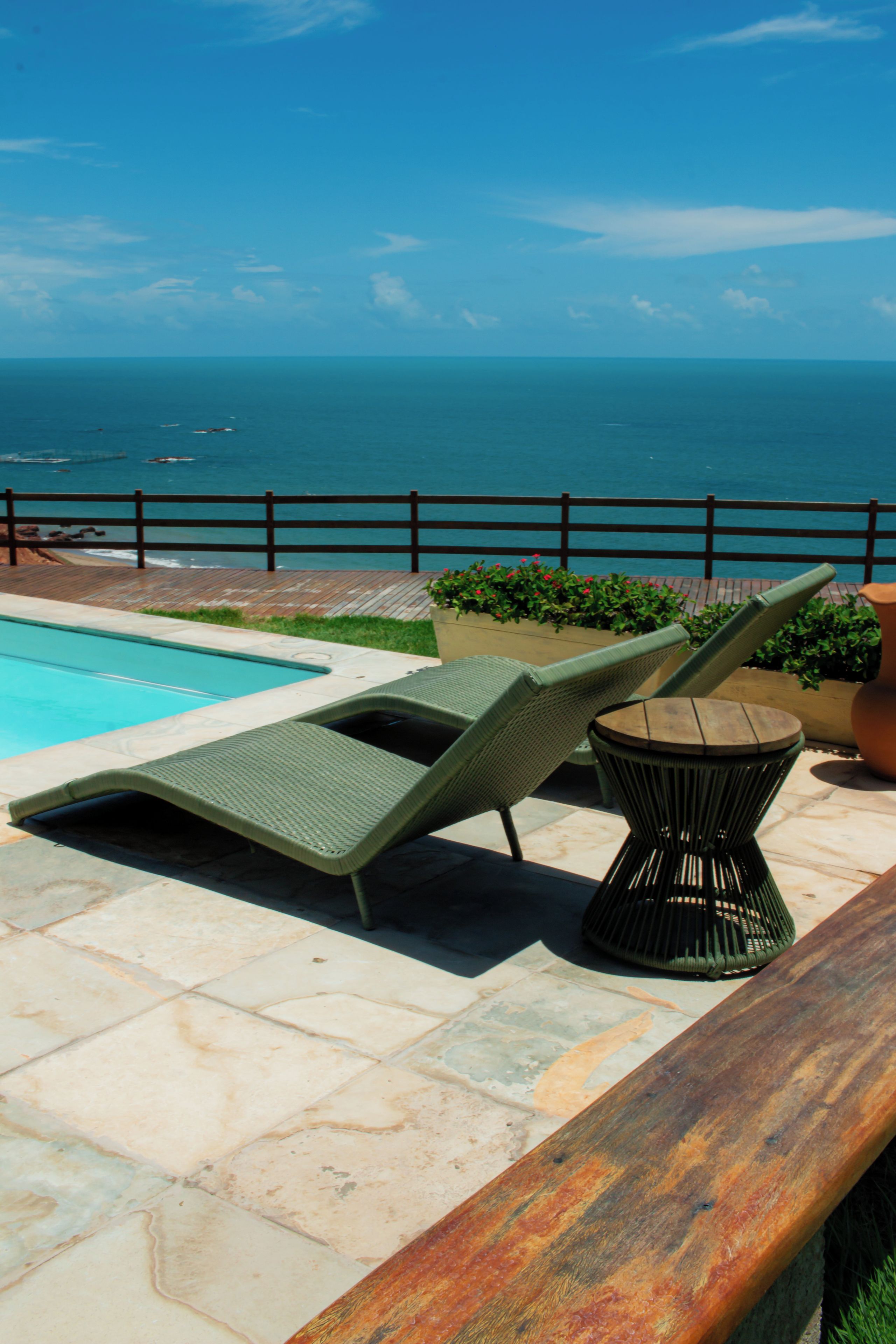 A poolside area with lounge chairs and a table, overlooking a body of water.