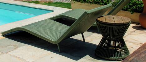 A poolside area with lounge chairs and a table, overlooking a body of water.