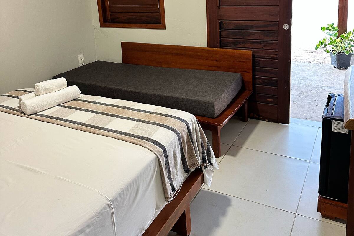 A bedroom with a bed, a bench, a wooden door, and a window.