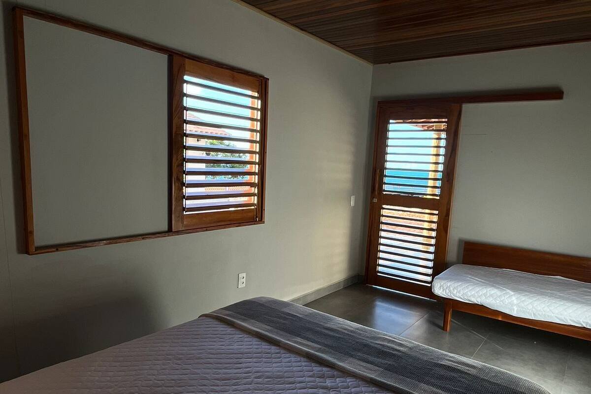 A bedroom with a large bed, two smaller beds, wooden ceiling, and windows with blinds.