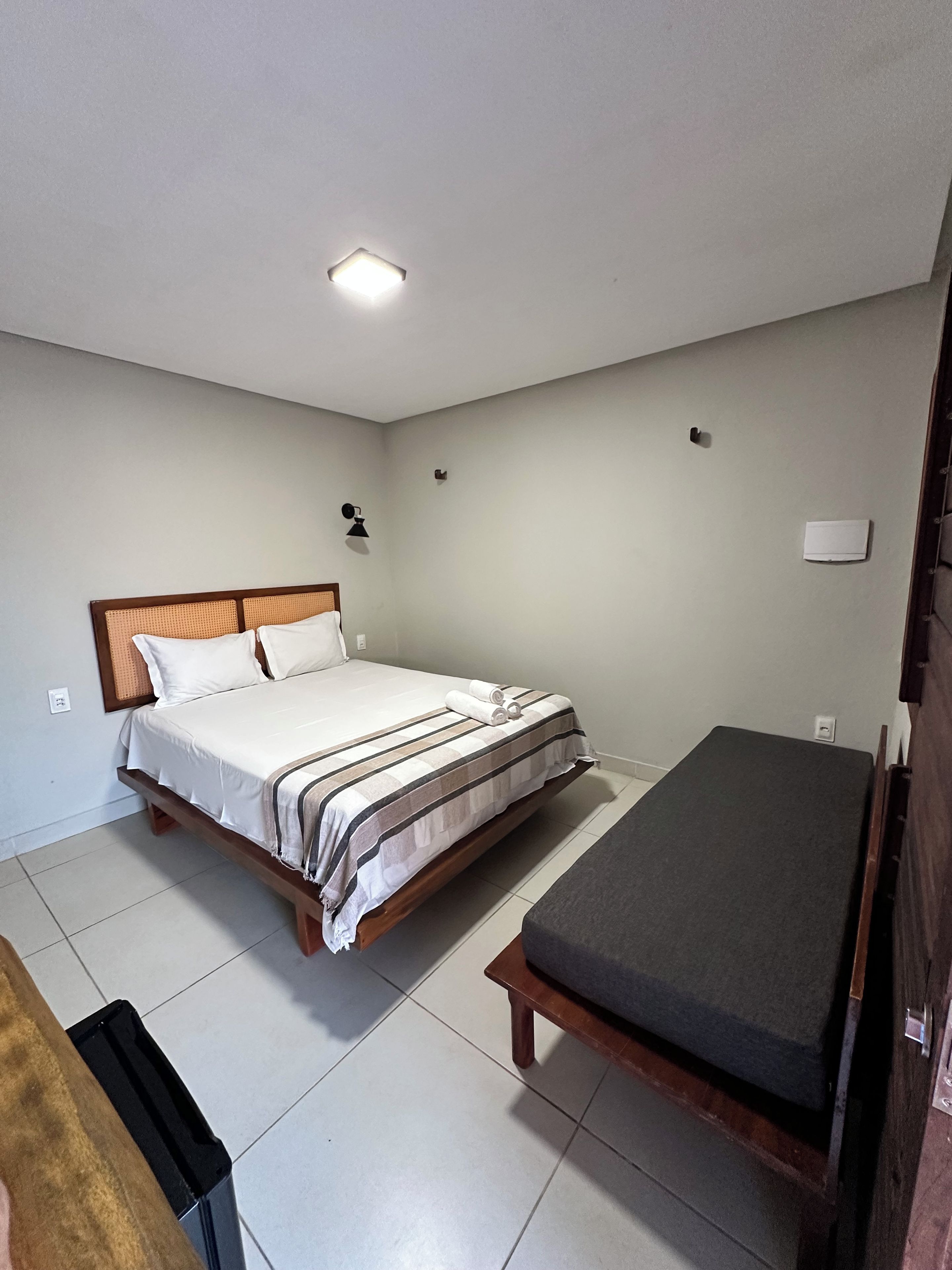 Una habitación con una cama, un banco y una lámpara en el techo.