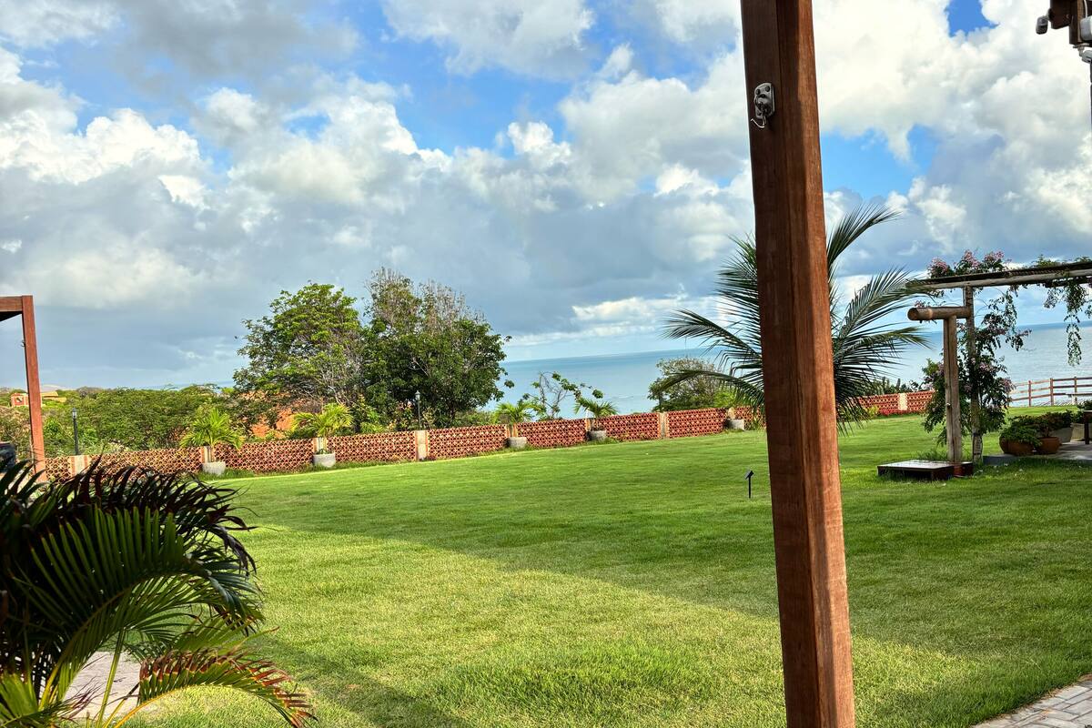 A covered outdoor area with a view of a grassy field and a wooden pergola.