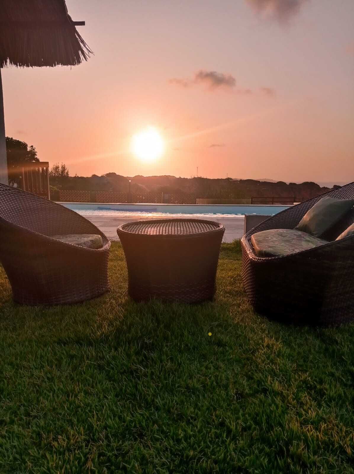 A sunset view with wicker lounge chairs and a pool.