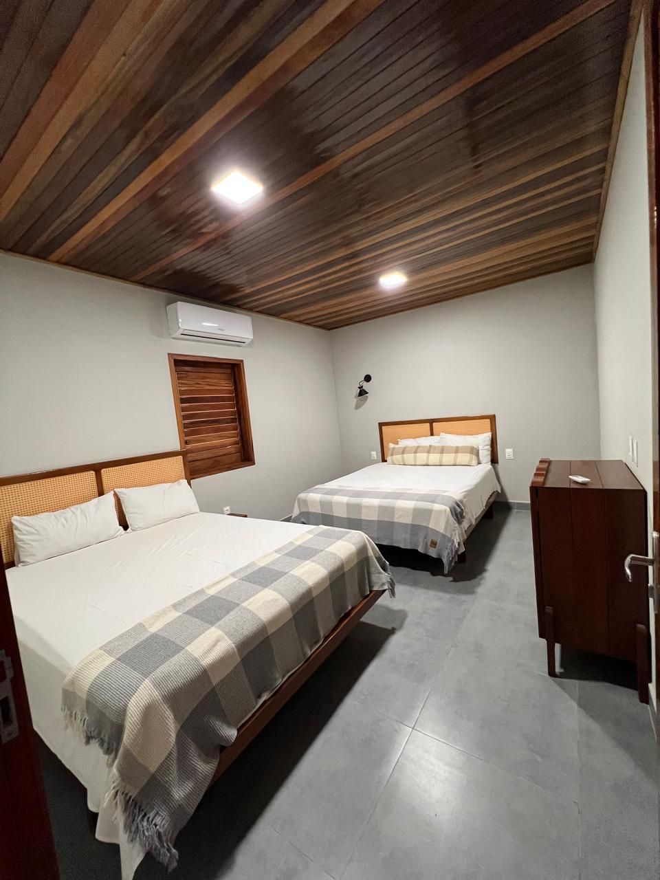 Un dormitorio con dos camas, techo de madera, unidad de aire acondicionado y un pequeño armario de madera.