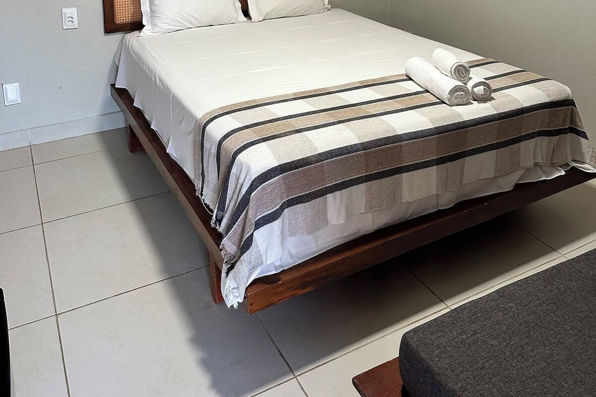 A neatly made bed with a striped bedspread, a wooden headboard, and a wall-mounted lamp.