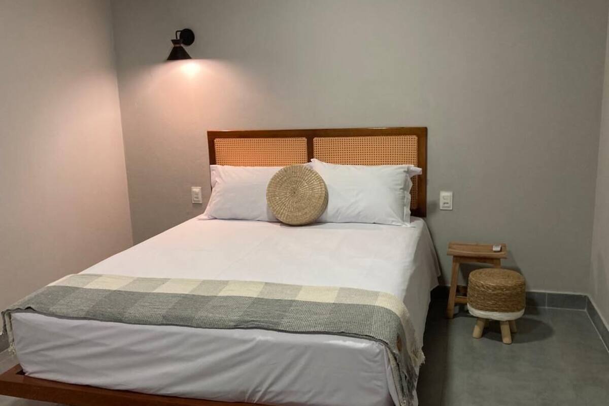 A neatly made bed with a wooden headboard, a bedside table, and a small stool.