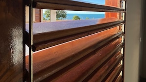 Vista a través de una ventana de listones de madera, con cielo despejado y paisaje lejano.