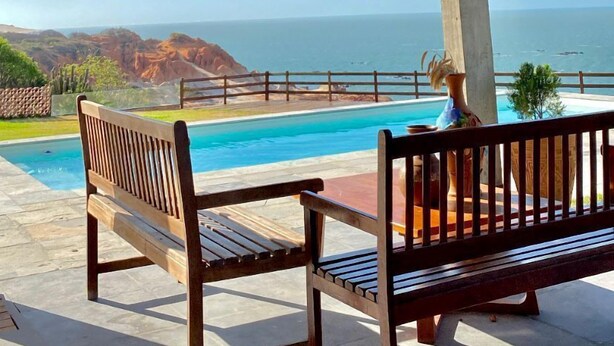 Un espacio exterior techado con piscina, bancos de madera y vistas al océano.