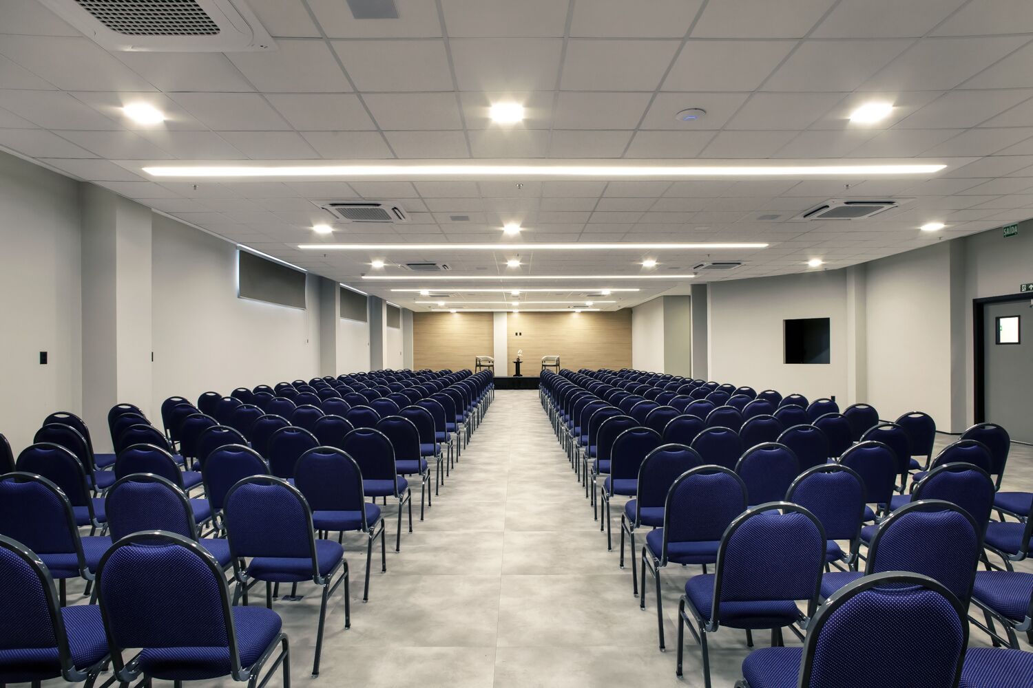 Ein Konferenzraum mit blauen Stühlen, einem Rednerpult und einem langen Tisch.