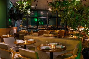 A restaurant with tables set for dining, large windows, and indoor plants. - NH Hotel Feira de Santana (Feira de Santana)
