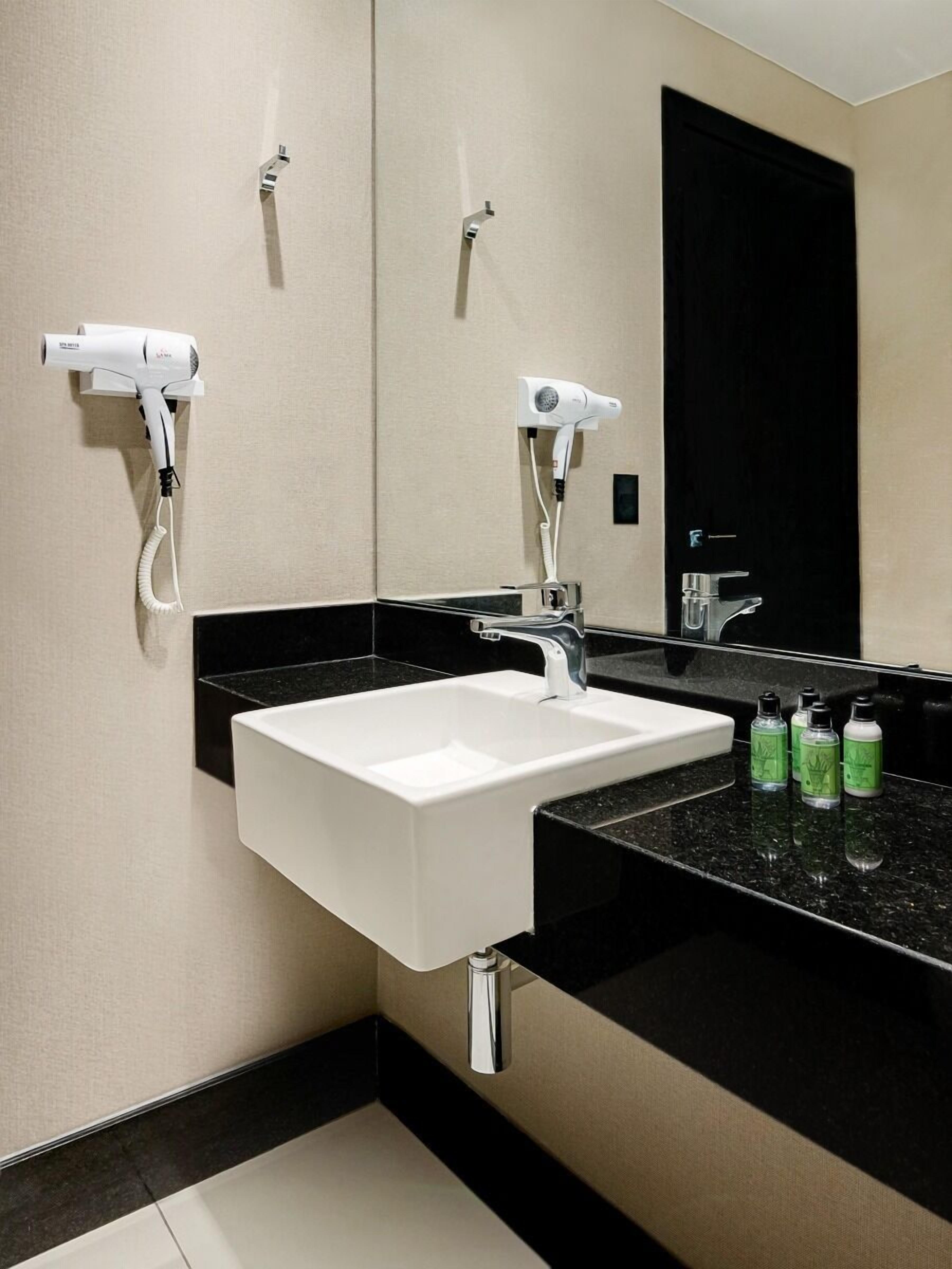 Une salle de bain moderne avec un lavabo blanc, un plan de toilette noir et deux sèche-cheveux fixés au mur.