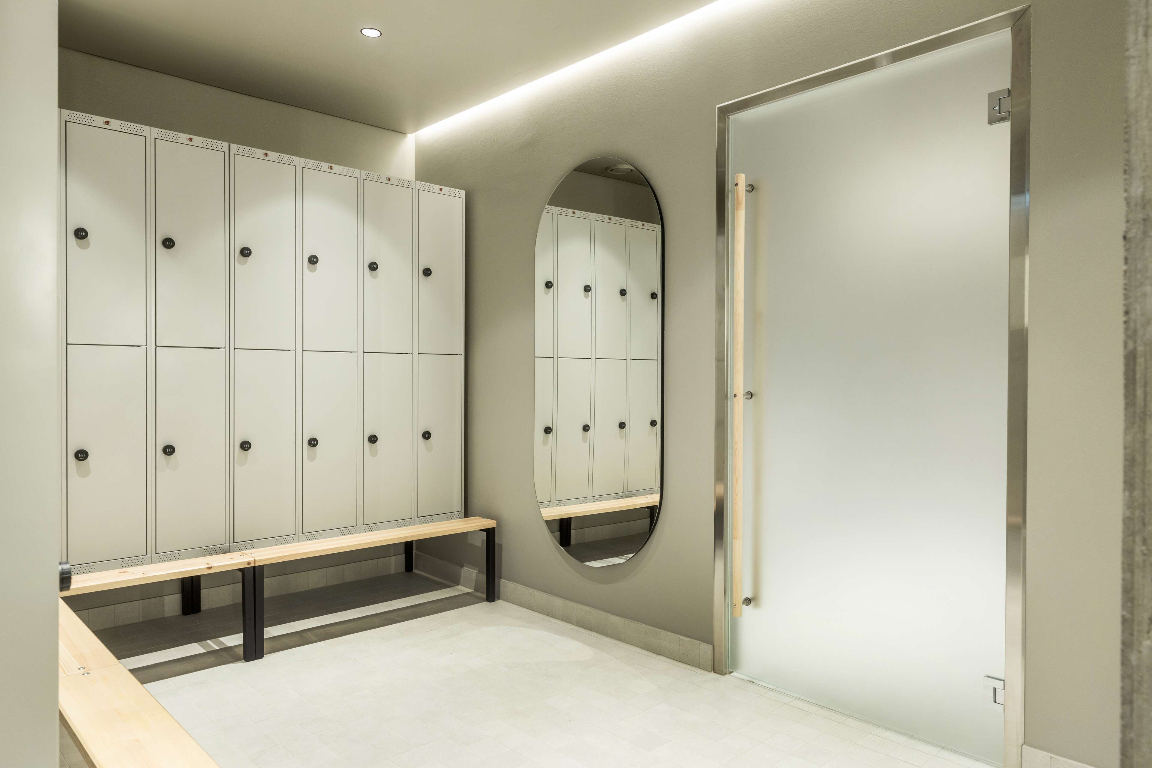 A locker room with multiple lockers, a bench, and a mirror.
